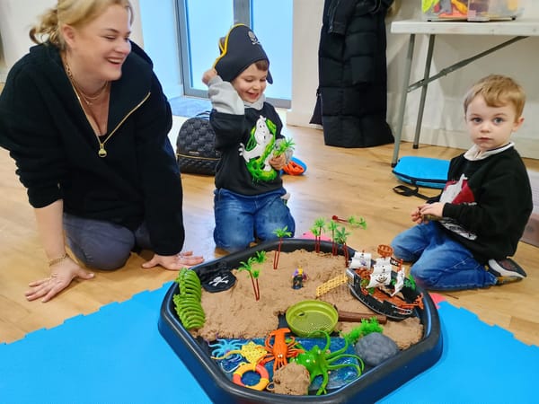 Photo of Rebecca McDermott with her children playing with toys in a sandpit